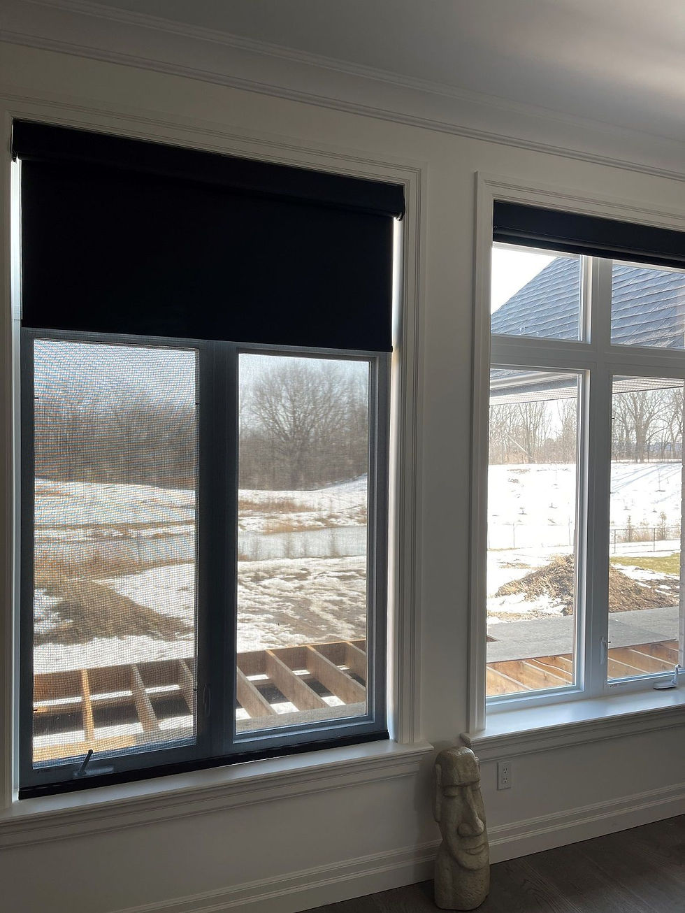 Angled view of two windows, one partially covered by a black window blind and one that is uncovered