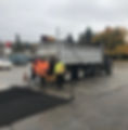 Workers laying asphalt in a parking lot with a truck behind