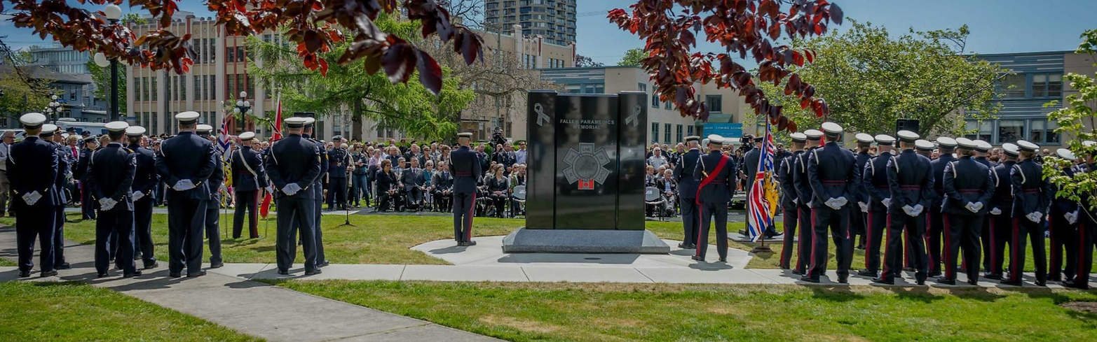 Naval officers stand in formation at a memorial ceremony outdoors on grass.