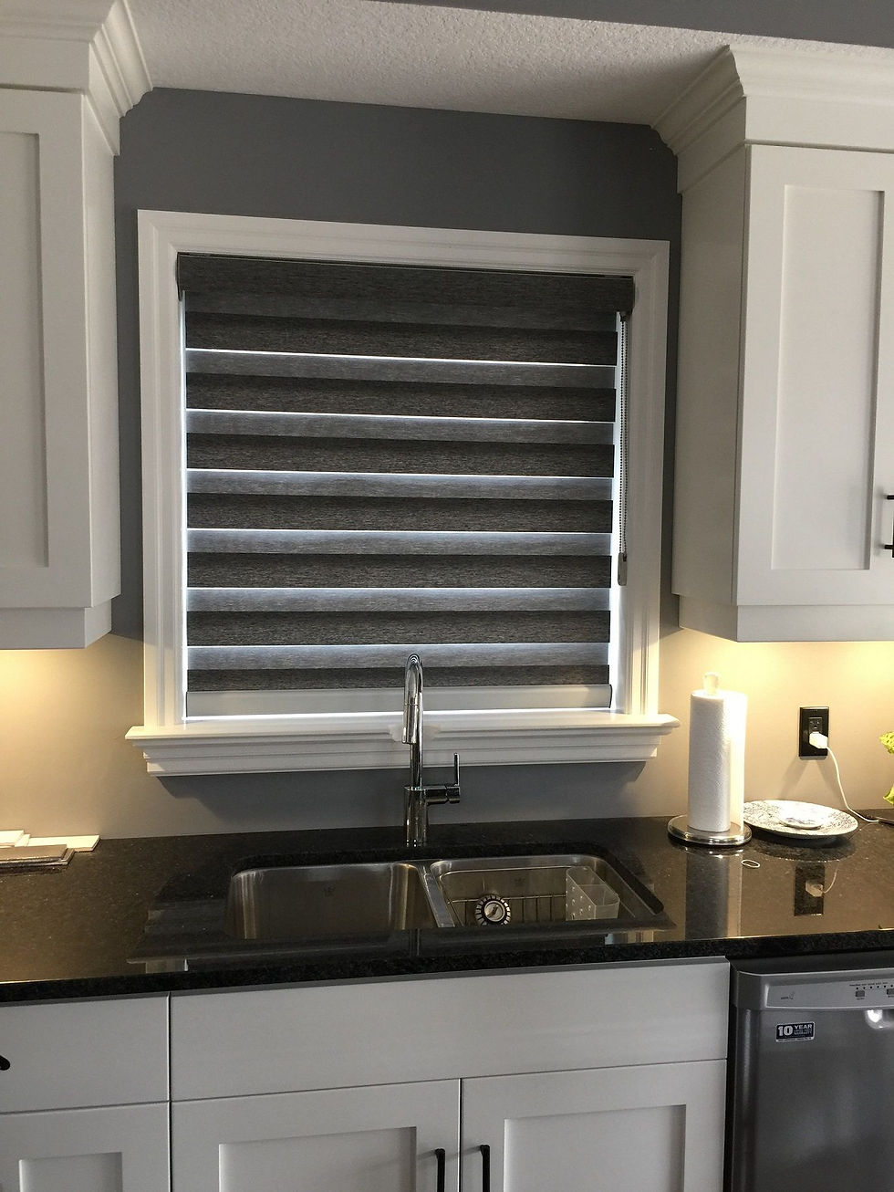 Front view of a kitchen window covered with a black pleated window shade