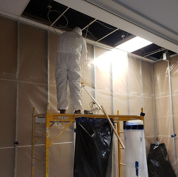 Worker in hazmat suit accessing ceiling wiring on scaffold