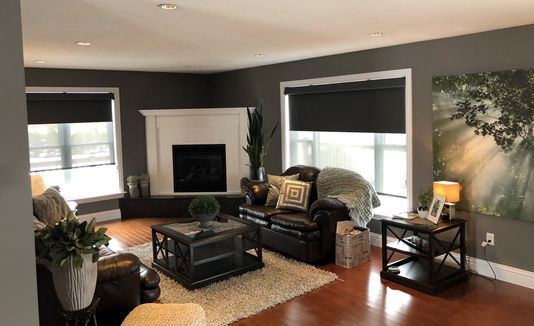 Wide angle view of a living room with two windows that are partially covered with blackout blinds