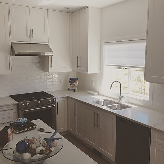 Interior view of a kitchen with windows, cabinets and countertop in colour contrast of white and brown. 