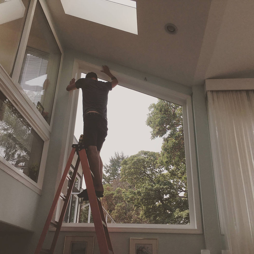 A man standing on a staircase installing a curtain on a window frame.