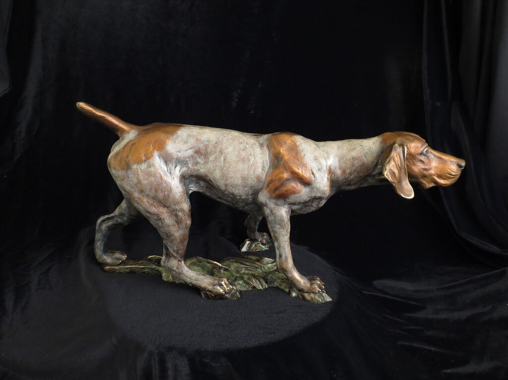 Bronze dog sculpture in hunting pose with details against black background.
