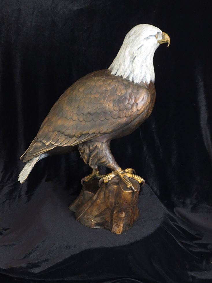 Bronze eagle statue perched on a wooden stump against a dark background, art