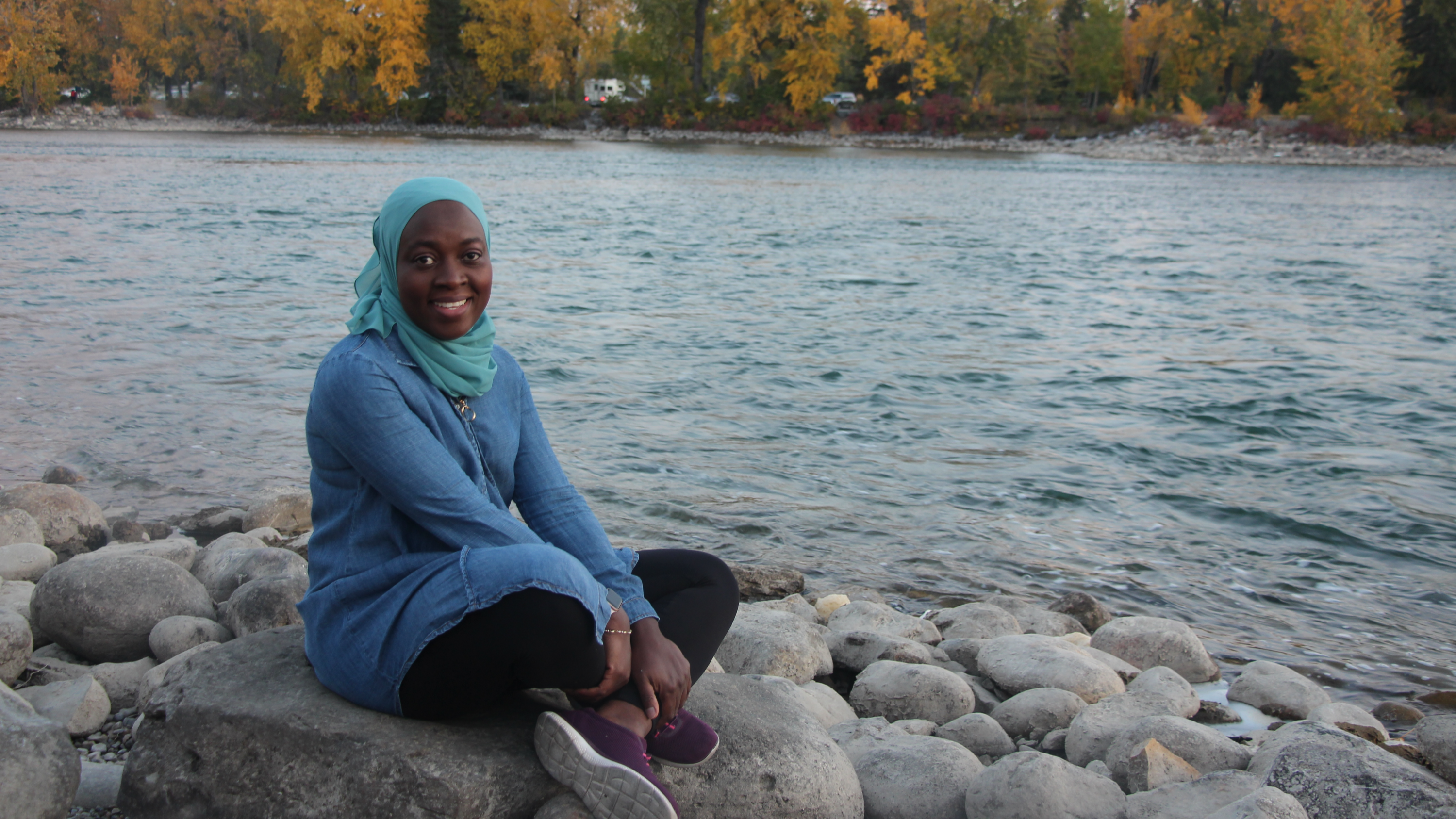 Sade sitting on rocks with a  gorgeous natural backdrop and lake surrounding her.