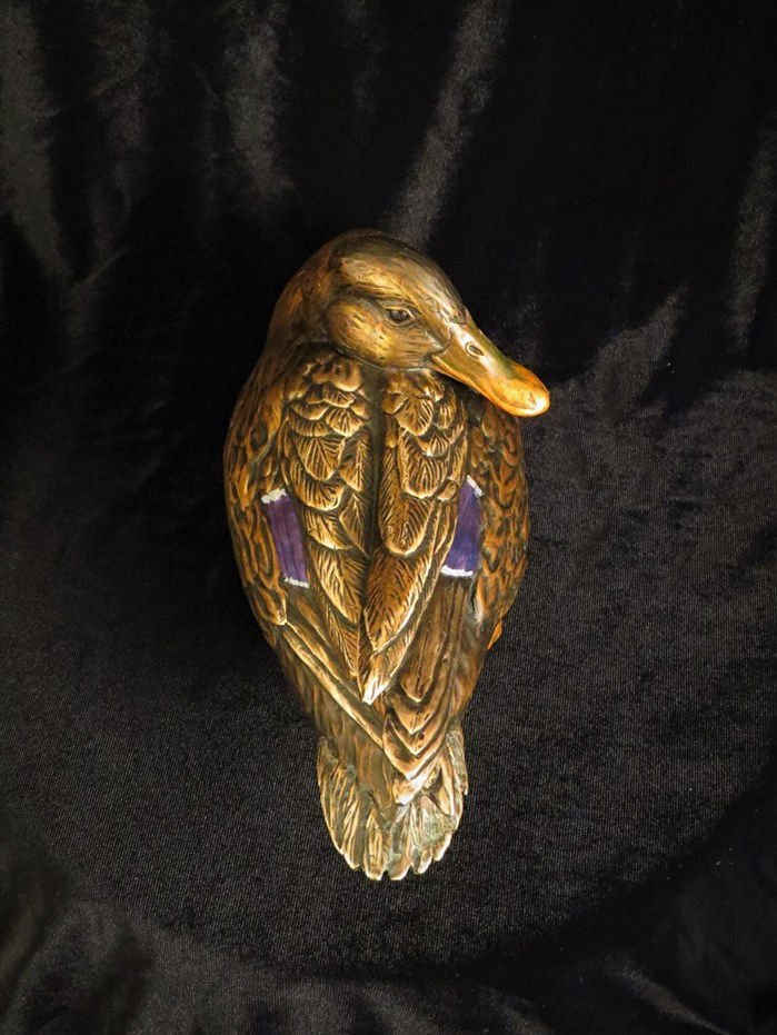 Golden duck statue, details visible, set against a dark velvet background.