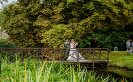 Bride and groom walk over the bridge together surrounded by trees and 