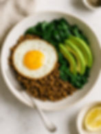 a savory breakfast bowl consisting of lentils, sautéed spinach, avocado slices, and a fried egg on top