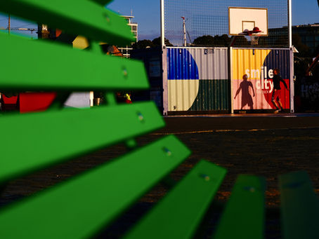Ein Streetfoto mit einer grünen Bank im Vordergrund, Silhouette im Hintergrund.