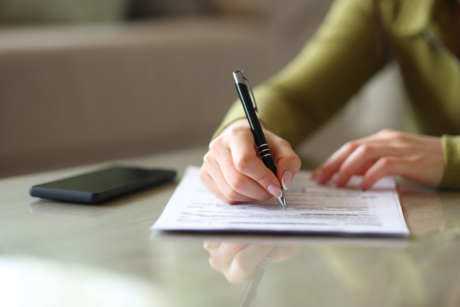 Close up of a beautiful woman hand filling out paper form on a coffee table.jpg