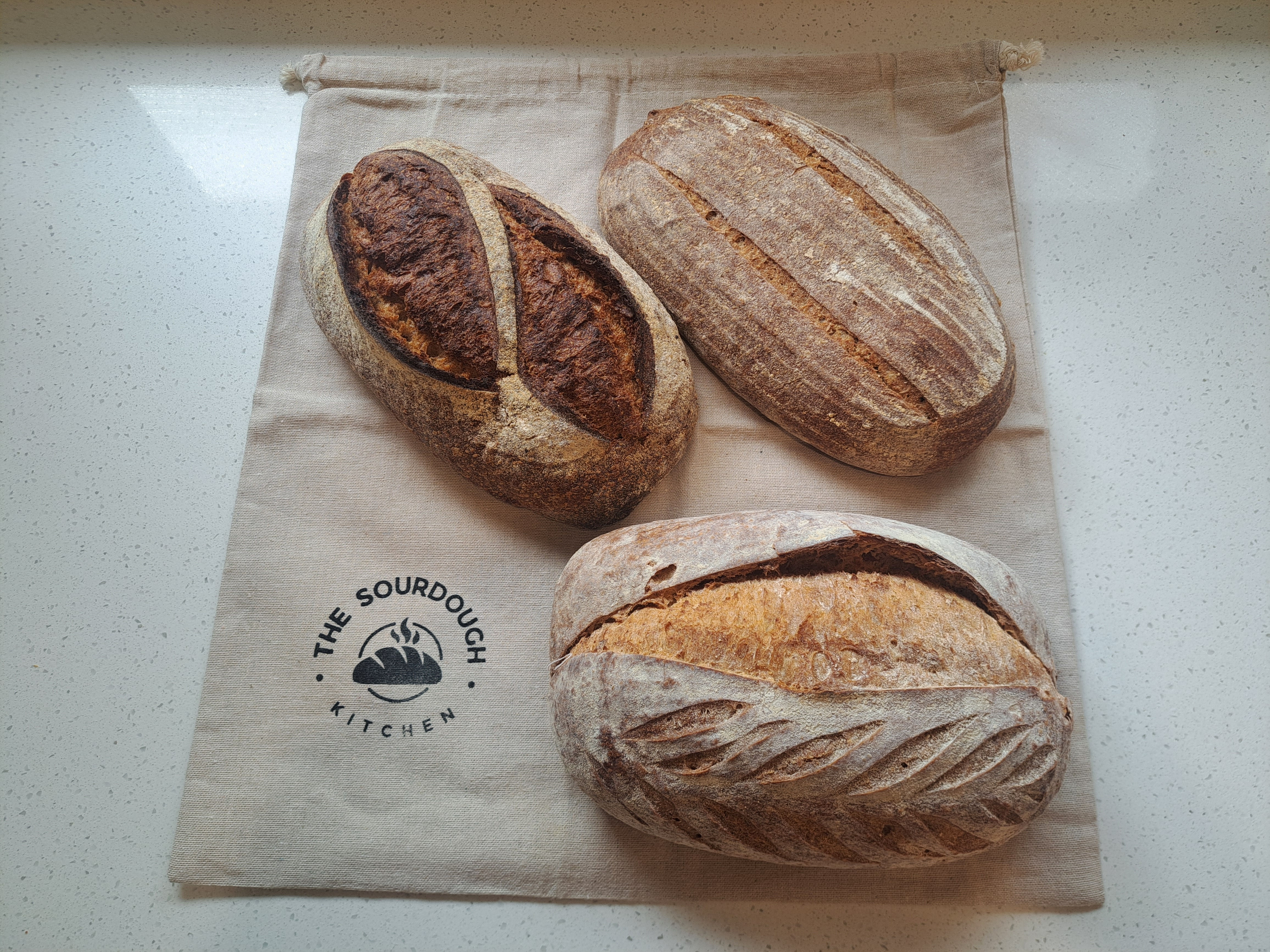 Three sourdough loaves arranged on an XL cotton bread bag with The Sourdough Kitchen logo.