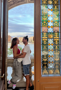 Barbi and Renato on a balcony at Buda Castle in Budapest with views of the Danube and the city center.