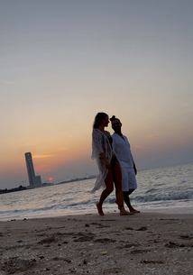 Barbi and Renato walking on the beach at sunset — calm lifestyle moment by the sea with skyline in the background.
