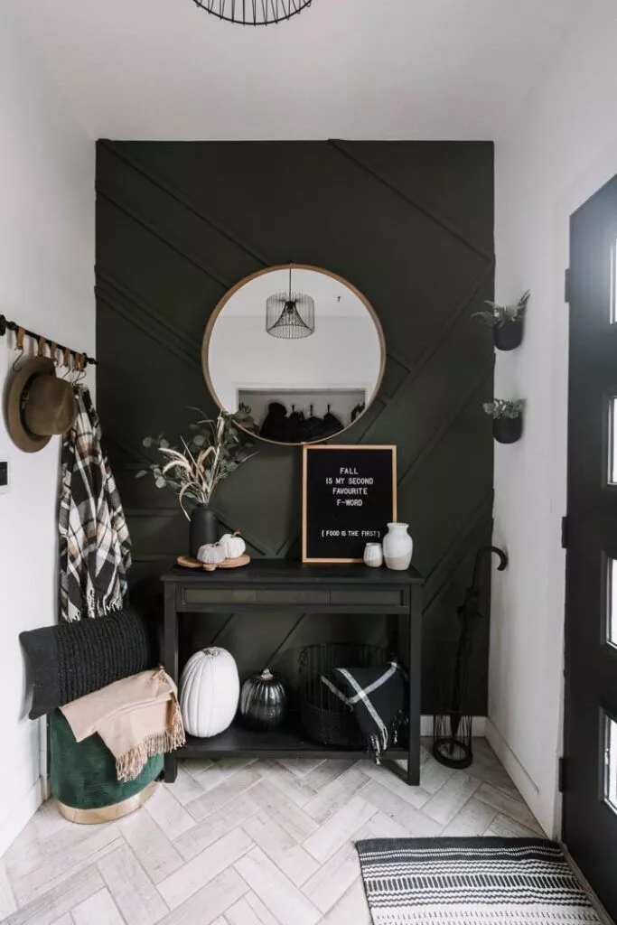 A dark coloured entryway fall decor with round mirror, pumpkins and more