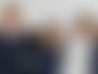 Seven smiling students in navy sweaters stand arm-in-arm against a white wall, exuding camaraderie and happiness.