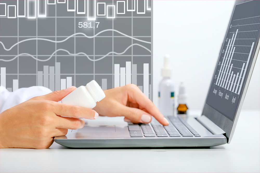 Person using laptop with prescription medication bottle in hand.