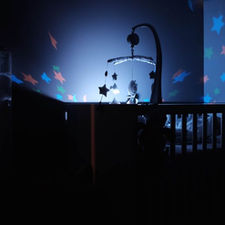 sleep training being taught in a dark nursery that has a crib, sparkle lights on the walls and a crib toy