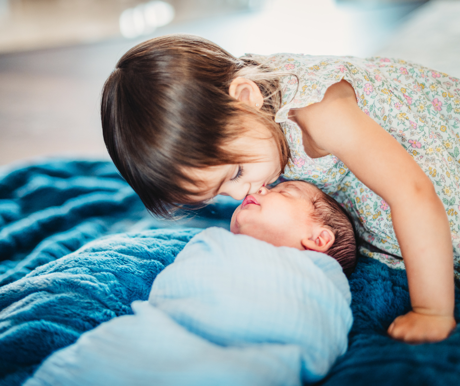 tiny newborn swaddled with a loving toddler kissing him on the nose