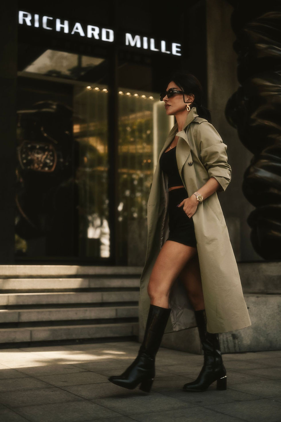 Woman in a beige trench coat and black leather boots on a city street
