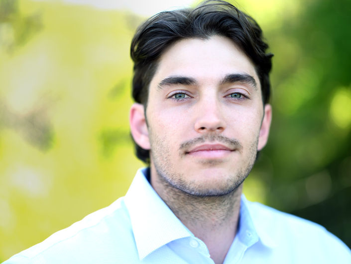 a portrait of a handsome young man with dark brown hair against a backdrop of green