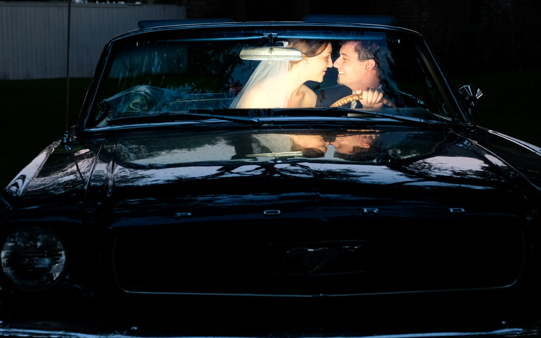 romantic wedding photo of the bride and groom sharing a kiss in their convertible classic car