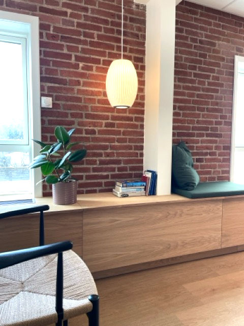 et venteværelse med murstensvæg, bænk i træ, plante og grøn pude