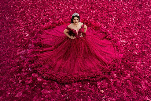 Quinceañera con un glamuroso vestido de color rojo sobre una capa de petalos color rojo