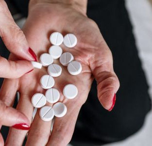 Händer med rött nagellack som håller i tabletter  