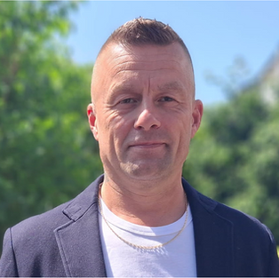 Thomas Lundblad som står i mörk kostym med vit T-shirt.