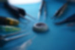 Surgical tools and needles encircle a lens on a blue surface, creating a focused and clinical atmosphere.