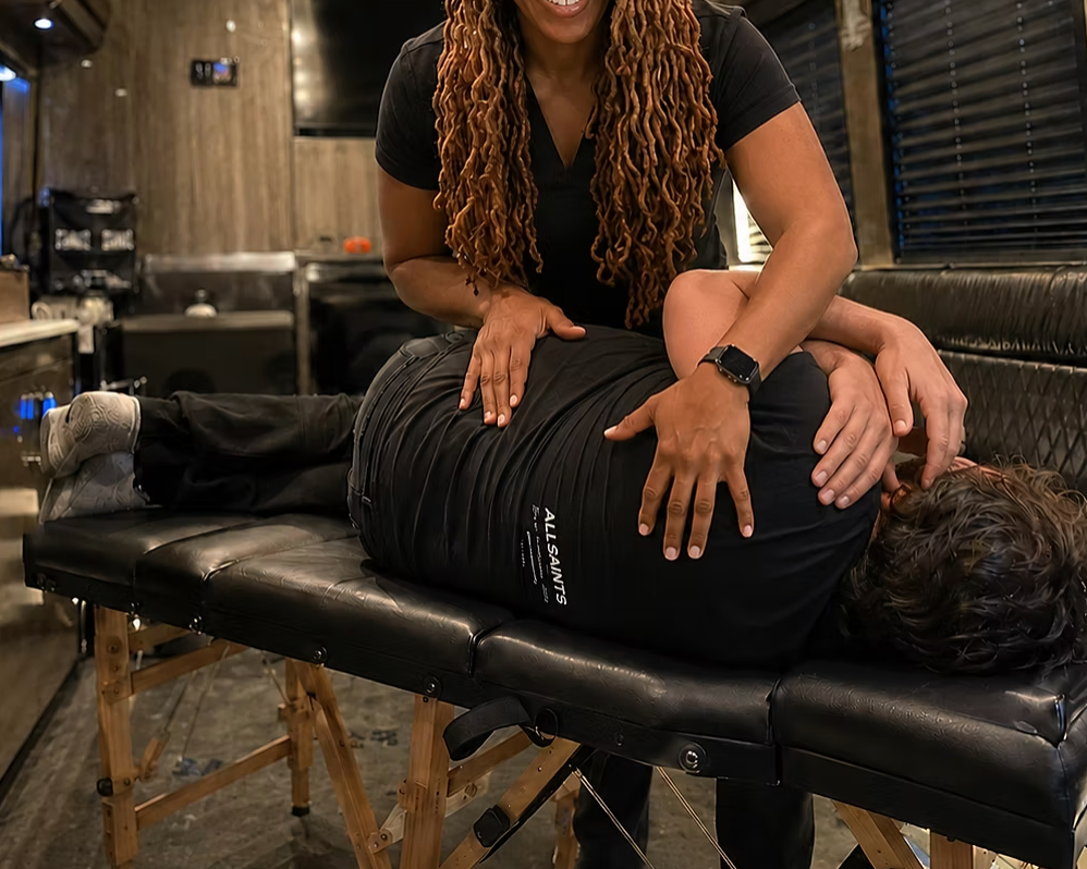 Chiropractor assessing a patient's back mobility during a personalized mobile chiropractic visit in a tour bus located in Baltimore
