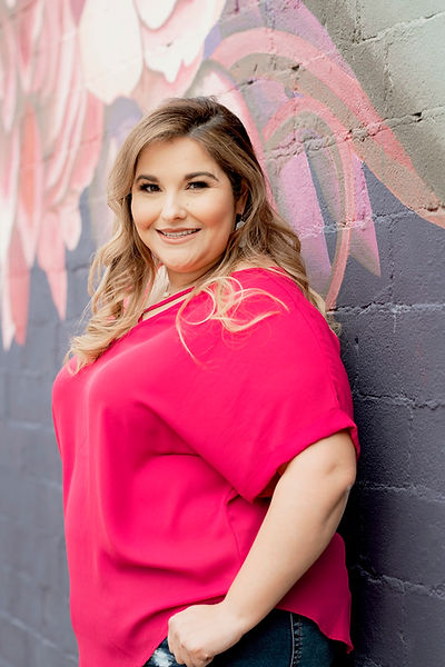 Hispanic blonde plus size woman smiling in front of a mural in houston wearing a pink blouse