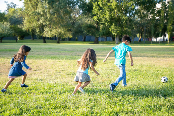 group-of-active-kids-playing-football-on-grass-in-city-park-full-length-back-view-childhoo