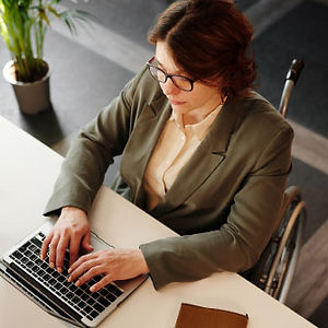 A young professional woman in a wheelchair types on a laptop in an office setting.