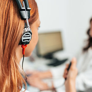 A woman with hearing impairment uses a microphone and headphones to communicate with a coworker.