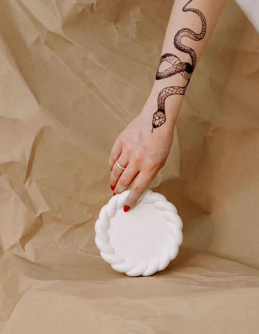 Hand with snake tattoo near white plate. Photography on brown surface.