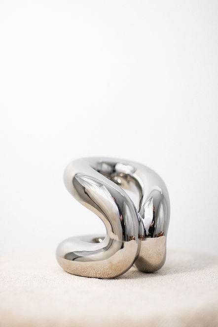 Metallic sculpture in the shape of a knot against a white background.