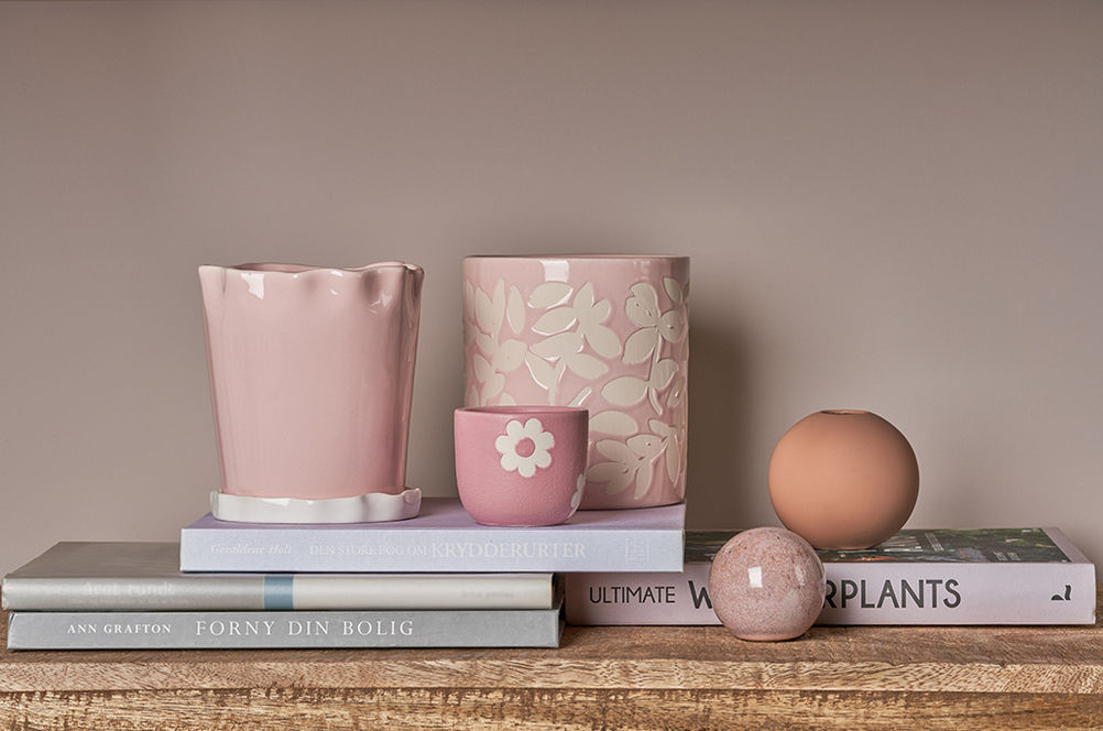Pink ceramic pots and spheres sit on books, floral design, background.