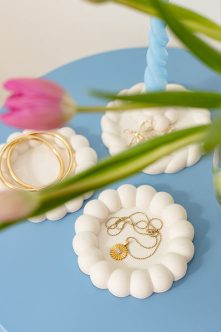 White ceramic flower-shaped dishes holding jewelry on light blue table Photography