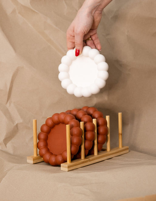 Hand holding a white plate, plates in wooden rack. Photography on brown background.