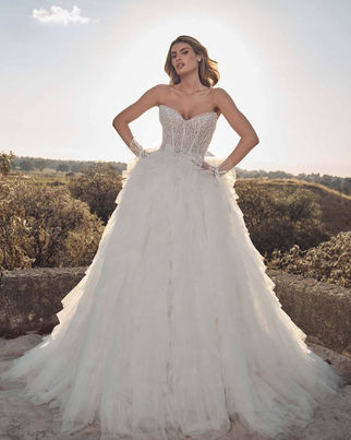 Rivienne STYLE  125248 Dress by Calla Blanche Bridal 
A strapless sparkly wedding dress like Rivienne knows how to steal the spotlight. From the sculpted semi-sweetheart neckline to the curve-hugging sheath silhouette, every inch is designed to dazzle with beaded lace and luminous detailing. For those craving drama, her voluminous detachable tulle overskirt delivers a showstopping moment—soft, romantic, and impossibly grand. Additionally, her matching gloves complete the look with couture-level flair, making this gown a glamorous fantasy from ceremony to reception.
Colors
Ivory/Light Nude (Pictured), Ivory/Ivory

Fabric
Lace, Beaded Lace, Tulle

Silhouette
Sheath

Neckline
Semi Sweetheart, Sweetheart, Strapless

Sleeves
Strapless/Sleeveless

Accessories (May Be Sold Separately)
Detachable Overskirt, Gloves

Style
Sparkly, Romantic, Glamorous, Statement

Size
0-24

Features
New Arrival, Sparkles
125248-Rivienne with detachable Skirt