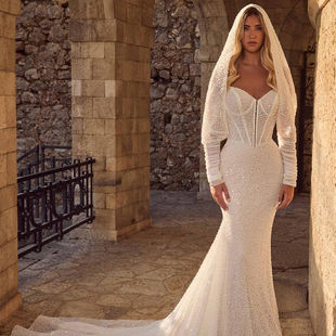 Ziva by Calla Blanche. Ziva is a show-stopping wedding dress that exemplifies high-fashion glamor. This sparkly sheath gown, adorned with beaded lace, embraces a romantic and luxurious aesthetic. Her sweetheart, strapless neckline brings a classic feel, while her unique long-sleeved hooded cape elevates the gown to a statement-making masterpiece. Perfect for brides wanting to make a grand entrance, this new arrival sparkles with every movement, offering a dazzling, modern edge to a timeless silhouette.