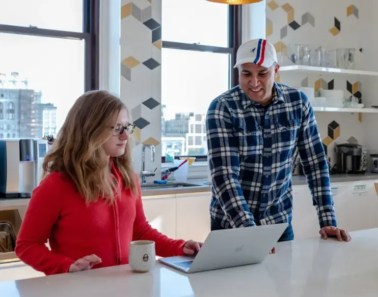 BrainPOP employees looking at a laptop in the BrainPOP office kitchen