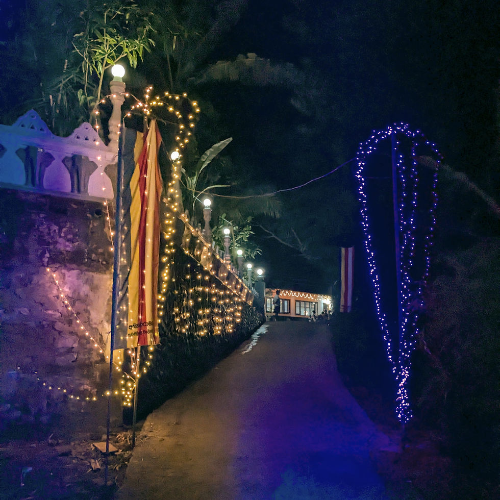 Nighttime photograph of a Buddhist temple beautifully decorated for Deepavali; the structure is outlined with rows of glowing oil lamps and string lights, casting a golden hue against the dark sky, with intricate patterns of illumination accentuating architectural details.
