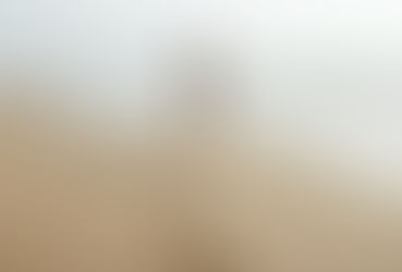 A woman in a white dress walks along a sandy beach, leaving a trail of footprints behind her. Though she doesn’t look back, the path she’s walked symbolises the essence of reverse goal setting—recognising how far you’ve come to inform where you’re going. Gentle waves and soft light create a peaceful, reflective mood.