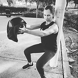 woman squatting against a pole holding a medicine ball