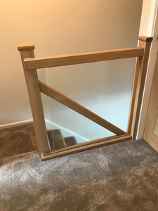 Modern wooden safety gate with clear glass panel above carpeted stairs.