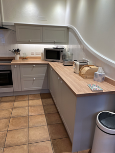 Light grey fitted kitchen with wooden worktops, microwave, and oven.
